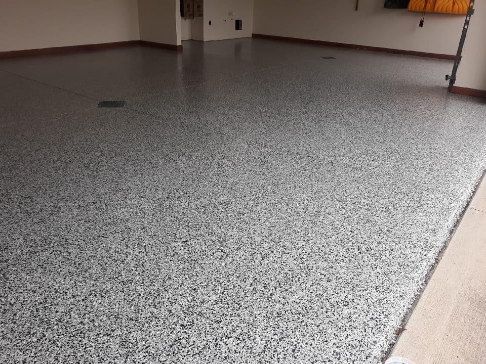 Epoxy-coated floor with gray and black speckled finish inside a commercial or garage space.