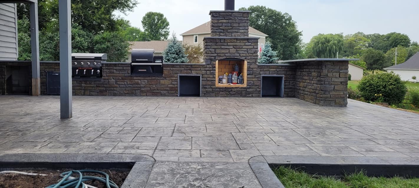 Stamped concrete patio with built-in stone outdoor fireplace and grill area in a residential backyard. Concrete patios in Monroeville. Concrete contractor in Ossian.