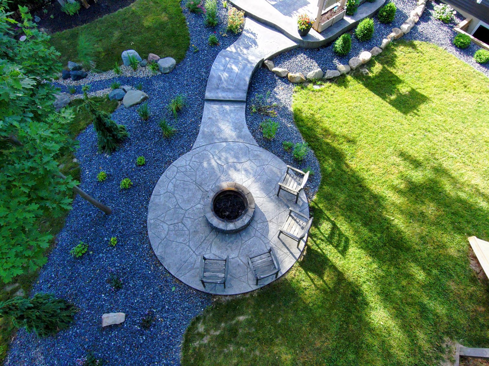 Aerial view of stamped concrete walkway leading to circular patio with fire pit and seating area surrounded by landscaped yard. Concrete patios in Paulding.