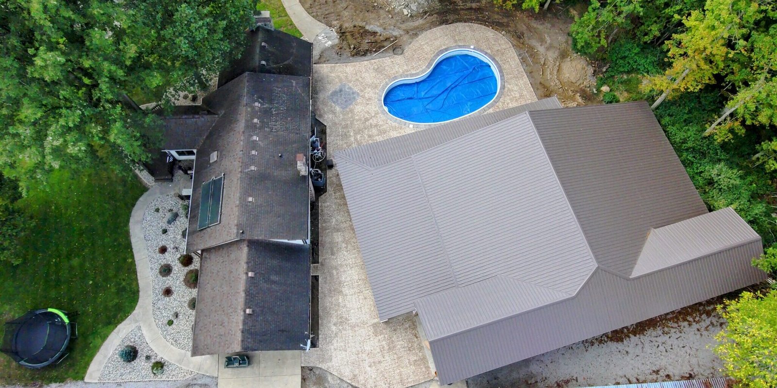 Aerial view of a residential property featuring a curved swimming pool, concrete patio areas, and surrounding greenery. Concrete Contractor in LaGrange