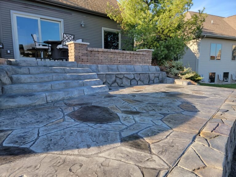 Stamped concrete patio with stone-textured steps leading to a raised outdoor seating area attached to a house.