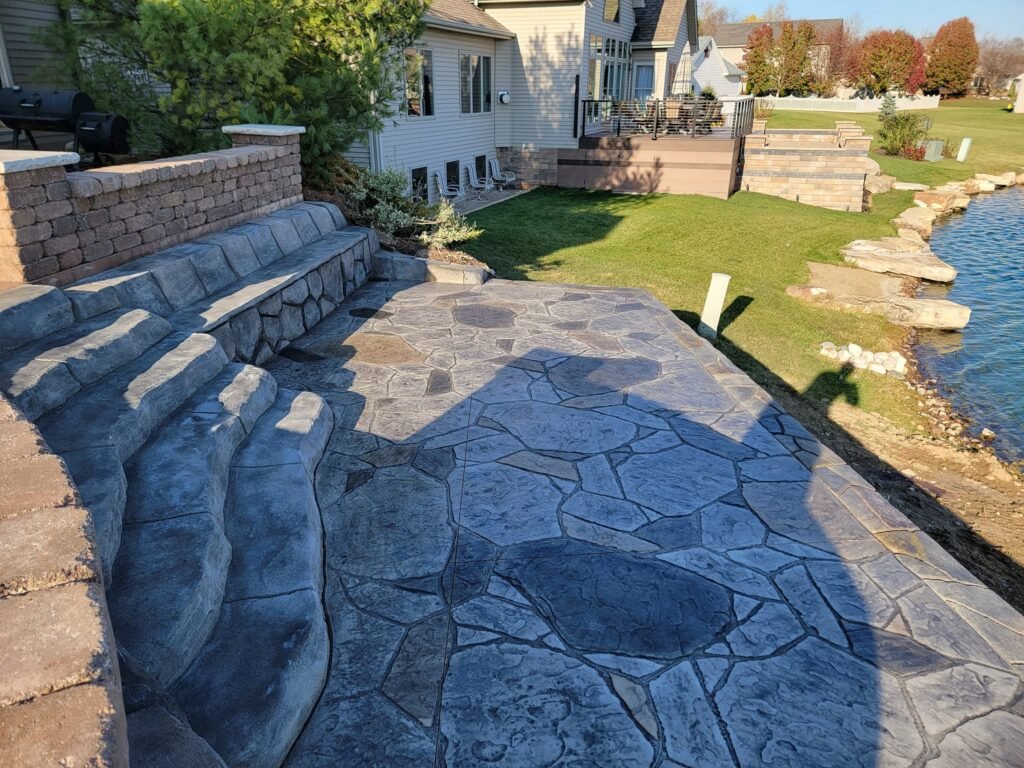 Flagstone-patterned stamped concrete patio with integrated bench seating and curved steps leading to a landscaped backyard. Concrete contractor in Leo-Cedarville. Concrete contractor in Decatur Stamped concrete in Ligonier.