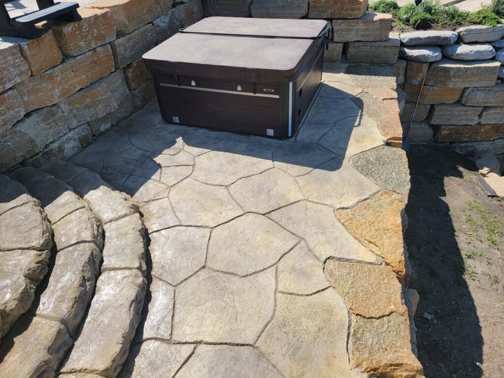 Stamped concrete patio with a flagstone pattern surrounding a covered hot tub and retaining wall. Stamped concrete in Warsaw. Concrete patios in Bryan