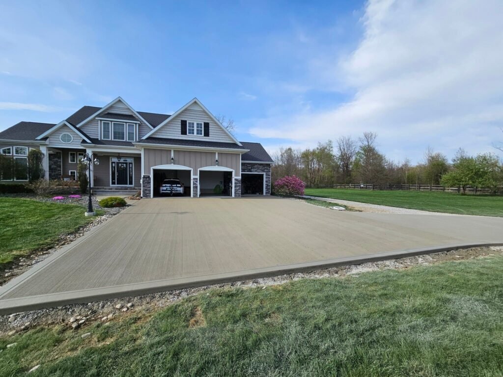 Freshly poured concrete driveway leading to a two-car garage in front of a modern suburban home, highlighting a clean, durable surface ideal for vehicle traffic. Driveway replacement in Monroeville. Driveway replacement in Huntertown.