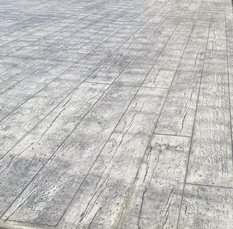 Close-up view of a stamped concrete surface with a wood plank pattern, featuring light gray tones and realistic grain textures for a natural, rustic look. Concrete contractor in Huntington.
