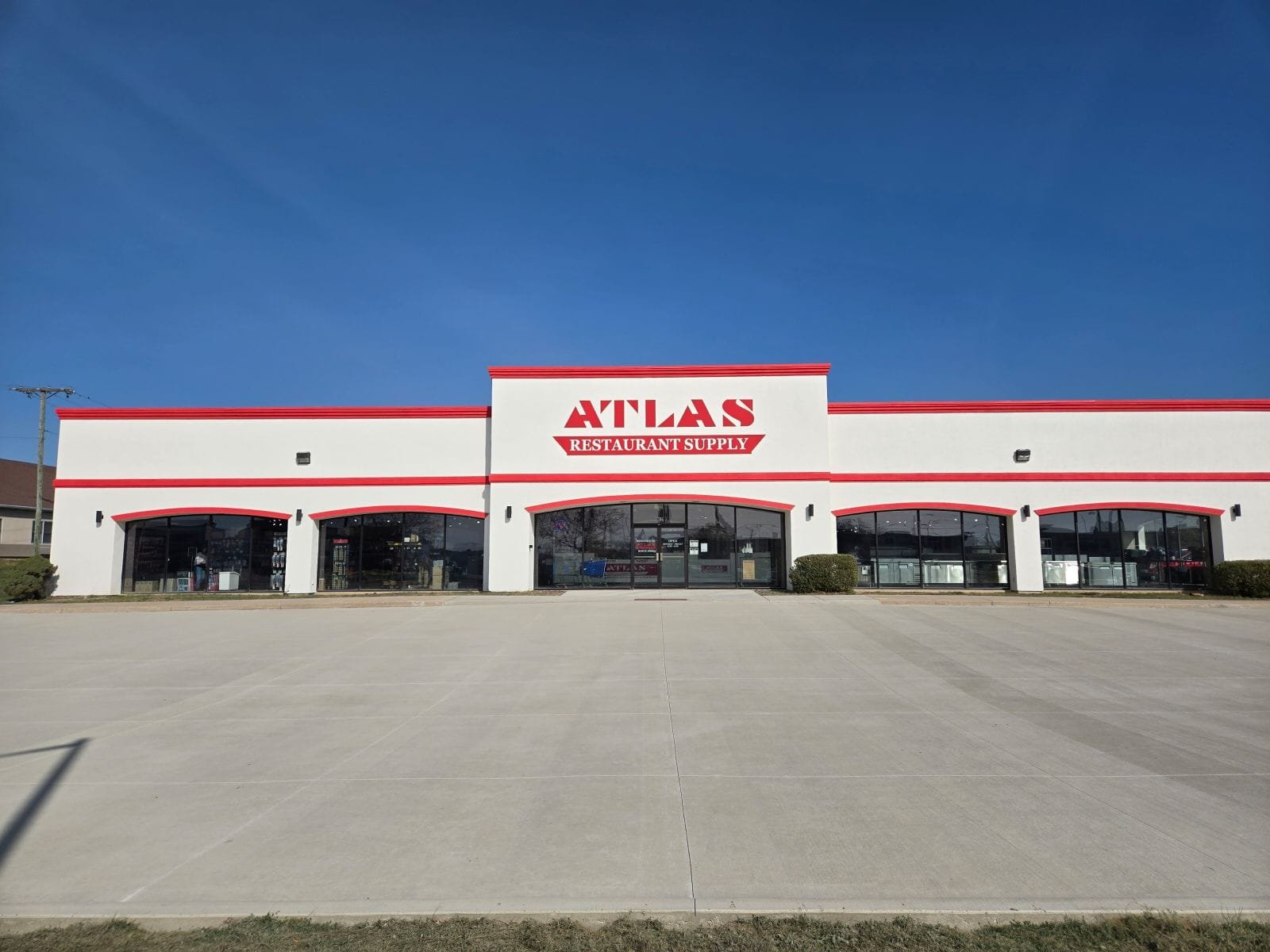 Exterior view of Atlas building supply storefront with clear signage and large parking area under a blue sky. Commercial concrete contractor in Avilla.