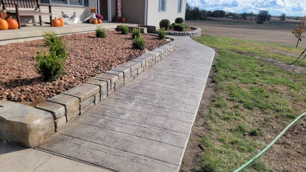 Curved stamped concrete walkway with a raised stone planter in Monroeville, Indiana.