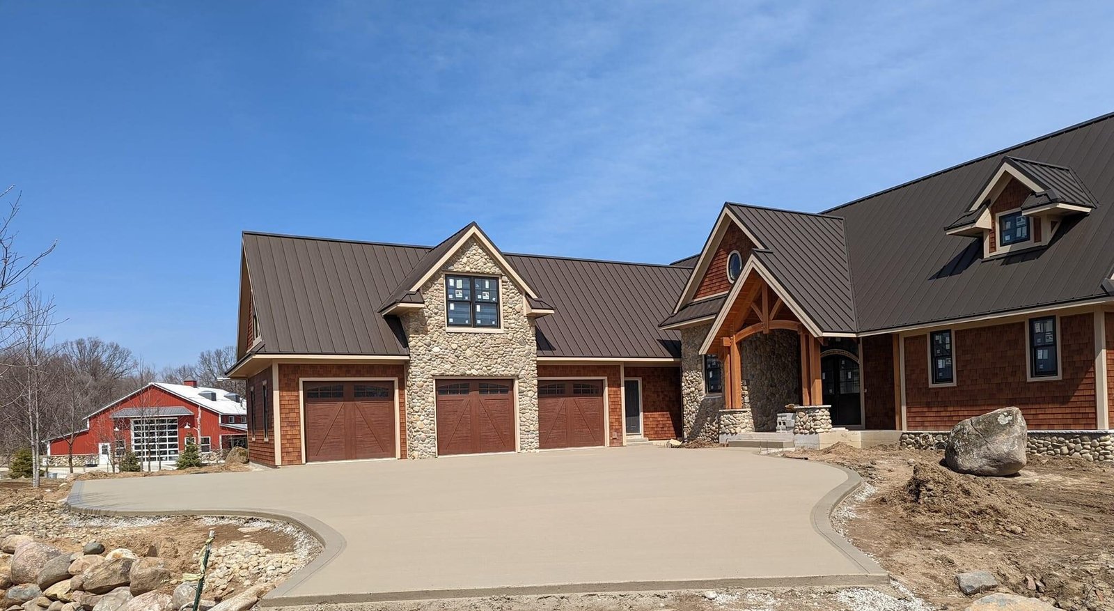 Newly poured concrete driveway in front of a large custom home with stone and wood exterior accents, surrounded by natural landscaping.