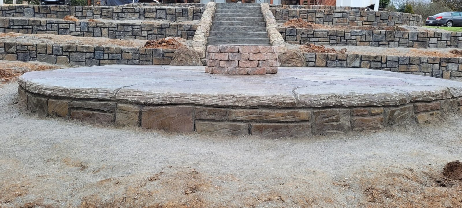 Outdoor stone staircase leading up to a raised patio with a circular stacked-stone fire pit in the center.