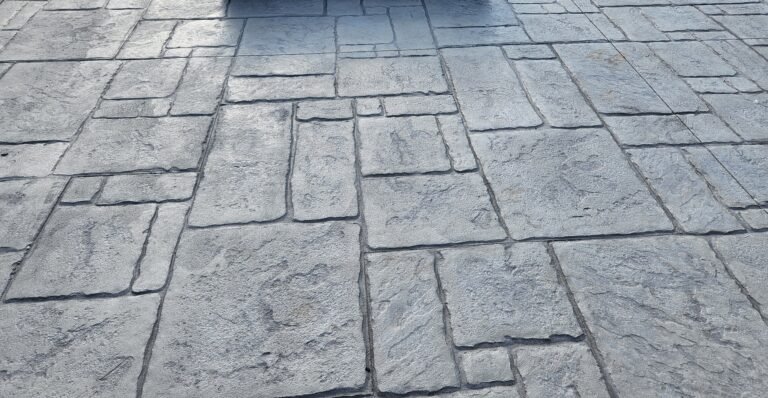 Stamped concrete patio with a square fire pit in the center, featuring a slate tile pattern in gray tones. Commercial concrete contractor in New Paris