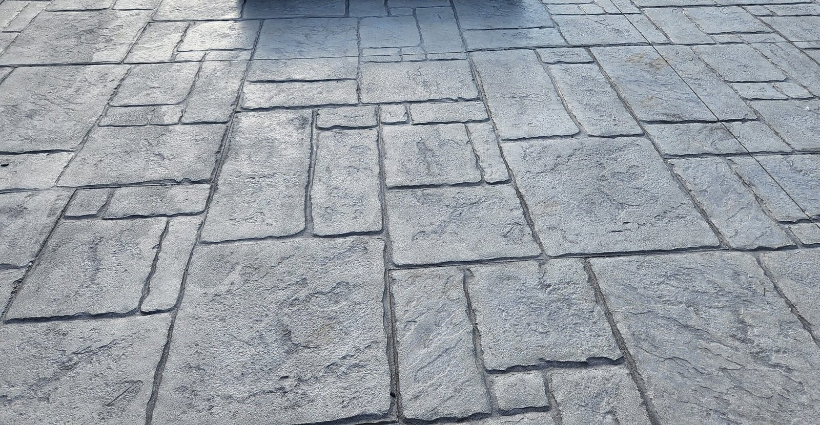 Stamped concrete patio with a square fire pit in the center, featuring a slate tile pattern in gray tones. Commercial concrete contractor in New Paris