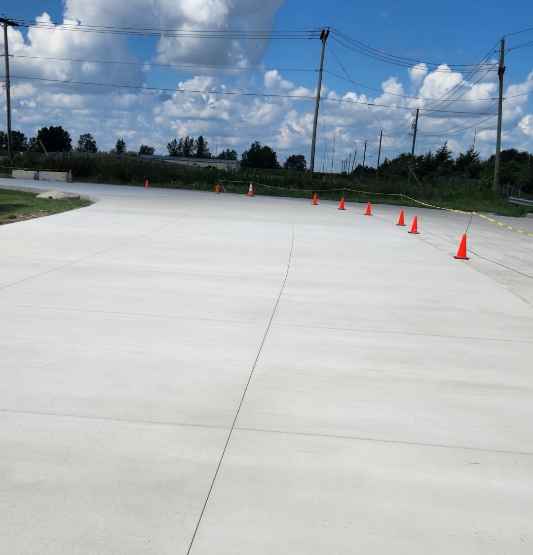 Commercial concrete contractor in South Whitley. Freshly poured concrete roadway or parking lot section with expansion joints and safety cones under a partly cloudy sky. Commercial concrete contractor in Hoagland. Commercial concrete contractor in Bluffton. Commercial concrete contractor in Bryan.
