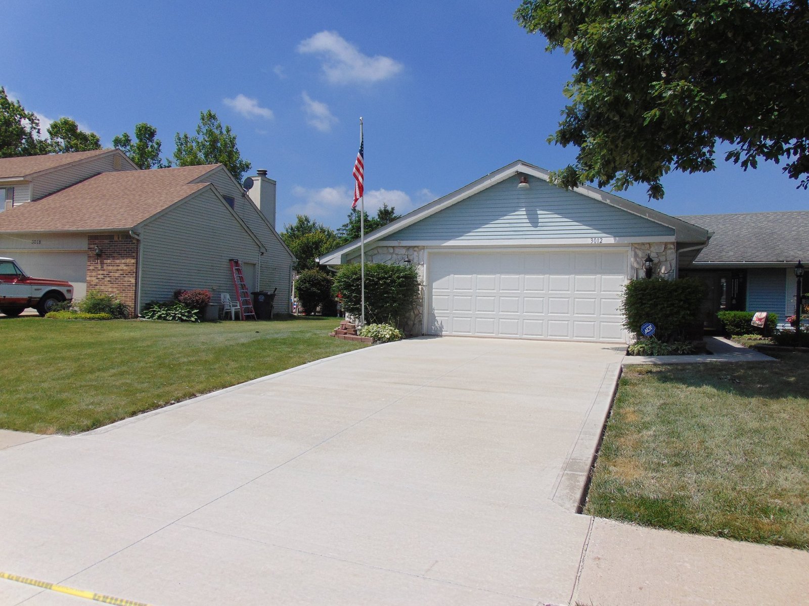 Smooth concrete driveway leading to a two-car garage with American flag and well-maintained front yard landscaping. Driveway replacement in Hoagland. Driveway replacement in Wabash.