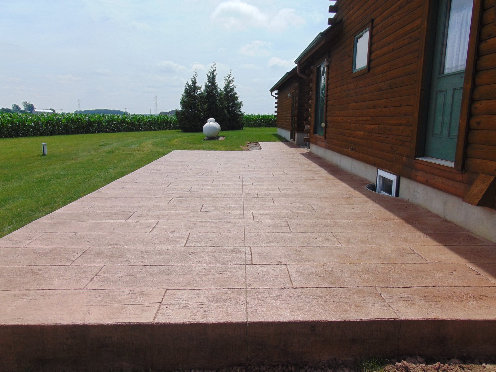 Brown stamped concrete long patio surrounded by green grass.