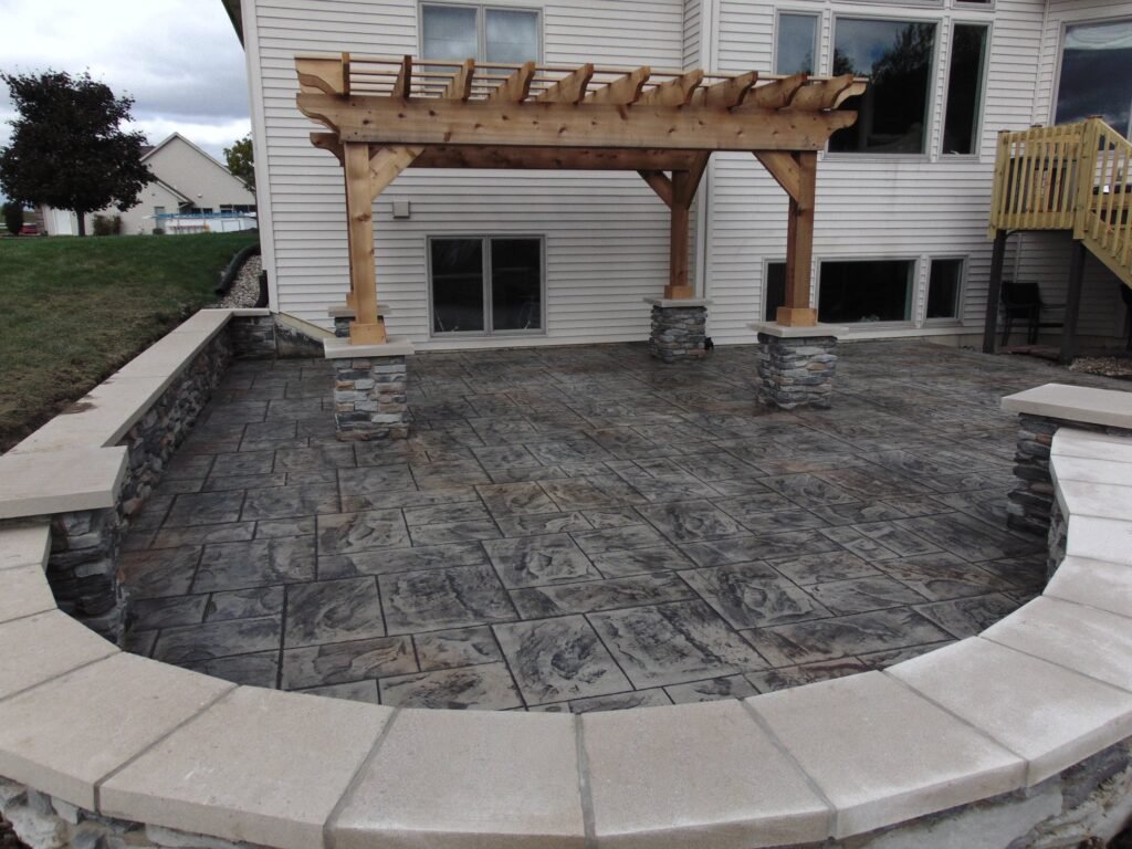 Elegant stamped concrete patio with a wood pergola and decorative seat wall, ideal for stylish backyard gatherings.