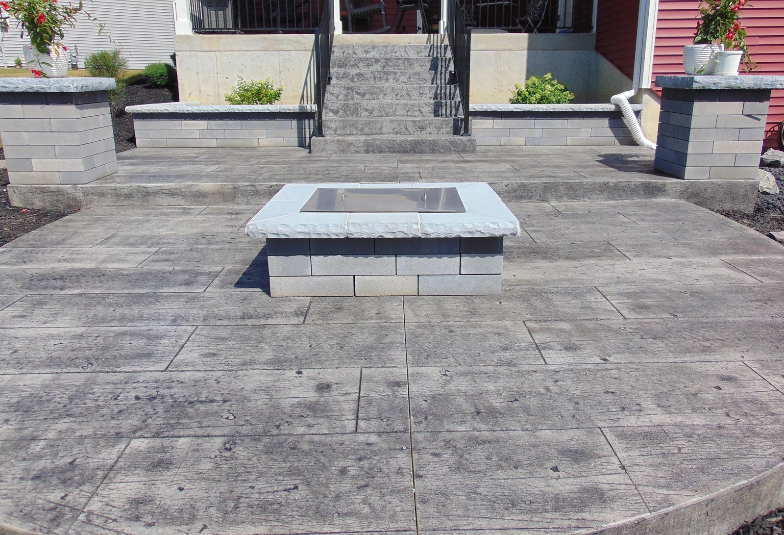 Stamped concrete patio with central fire pit and decorative retaining walls leading up to a home’s entry steps.