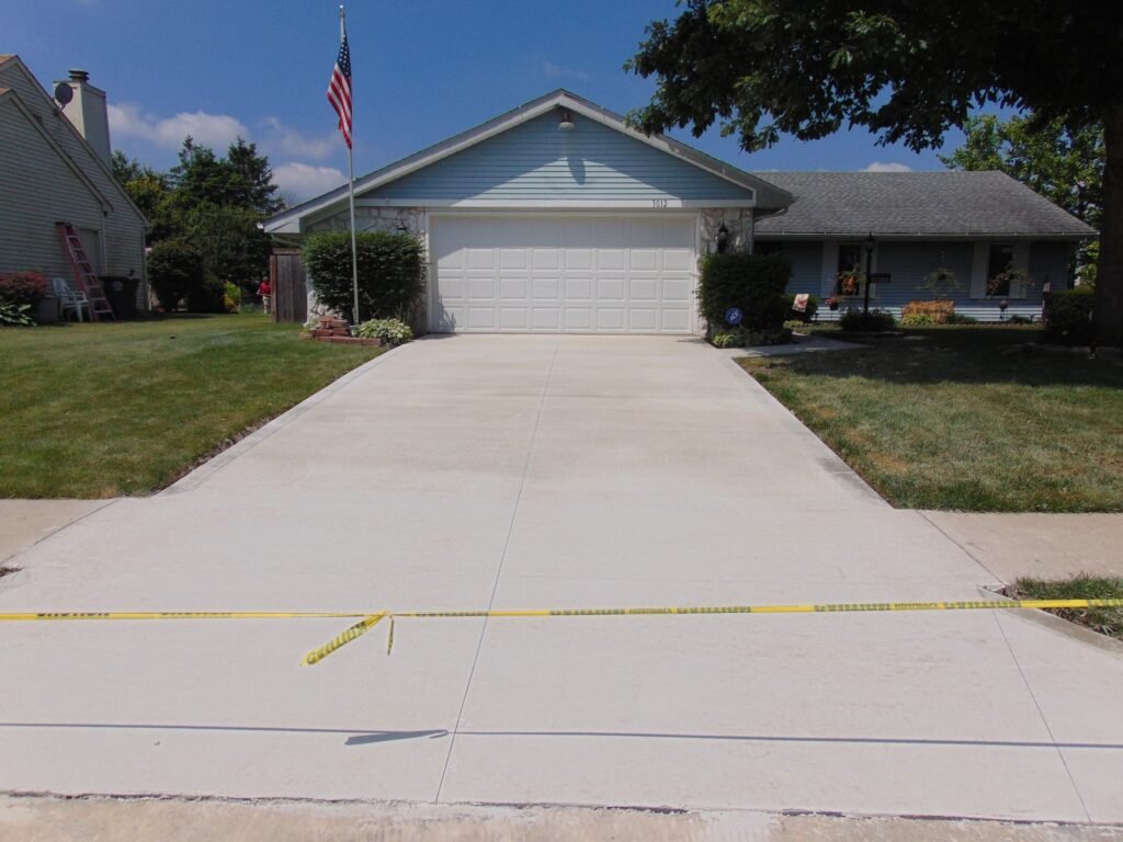New broom-finished concrete driveway curing after replacement near Fort Wayne, Indiana.
