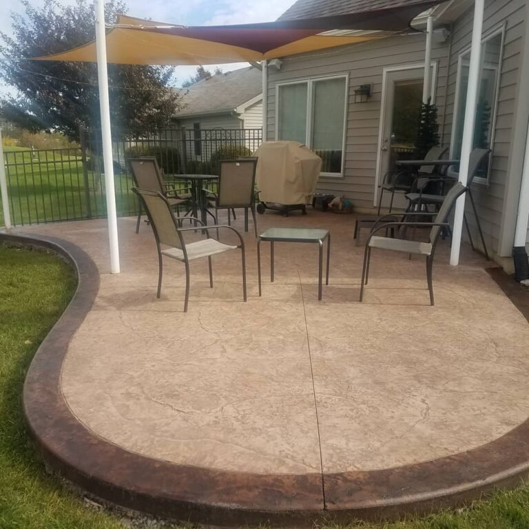 Curved stamped concrete patio with seating and a shade sail in Hoagland, Indiana.