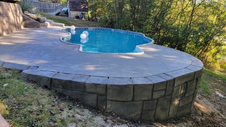 Concrete spa with a rounded edge and built-in bench wall in a wooded backyard