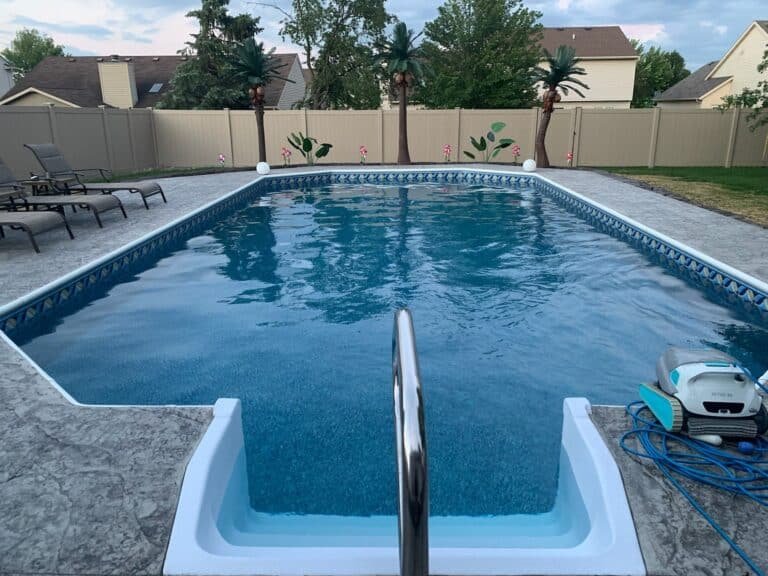 Inground pool with a textured concrete deck and privacy fence