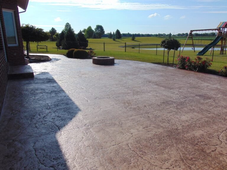 Large stamped concrete patio with a stone fire pit overlooking a pond