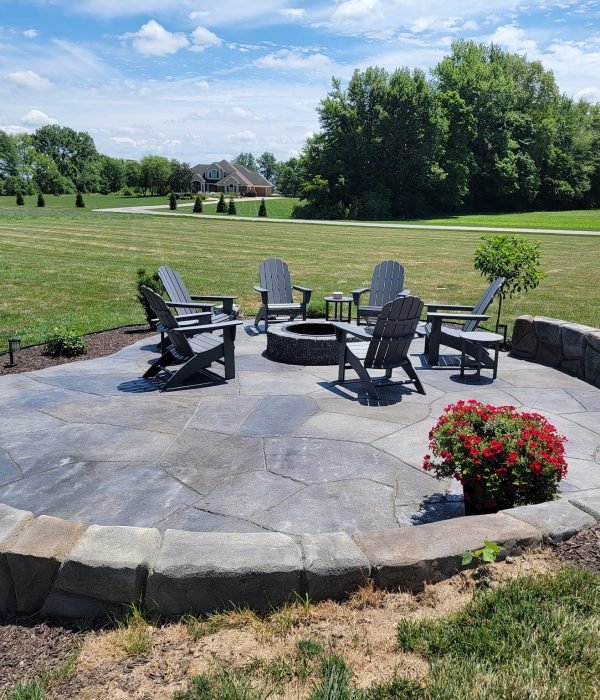Concrete patios in Fort Wayne. Circular stamped concrete patio featuring a built-in fire pit and curved seating wall, set against an open grassy landscape.