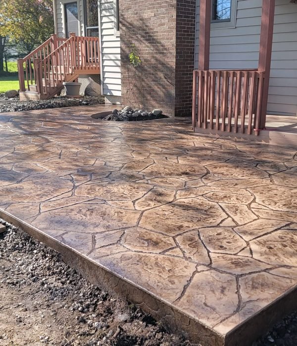 Stamped concrete patio with rich texture and warm tones, designed to extend outdoor living space adjacent to a home’s back entry.