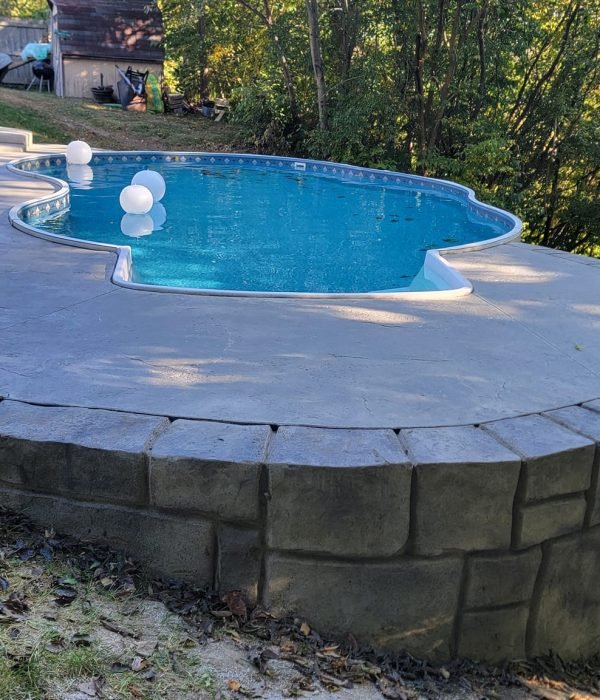 Custom concrete spa with rounded edge and built-in retaining wall bench, set in a wooded backyard for private relaxation. Concrete patios in Huntertown.