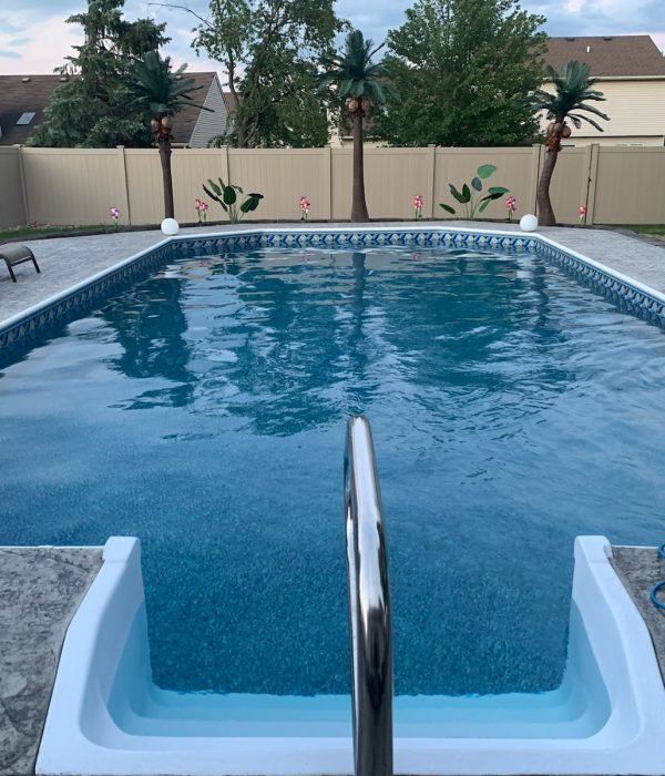 Rectangular inground pool with textured concrete pool deck and privacy fence, offering a clean and functional outdoor swimming area.