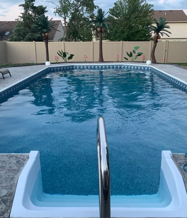 Rectangular inground pool with textured concrete pool deck and privacy fence, offering a clean and functional outdoor swimming area.