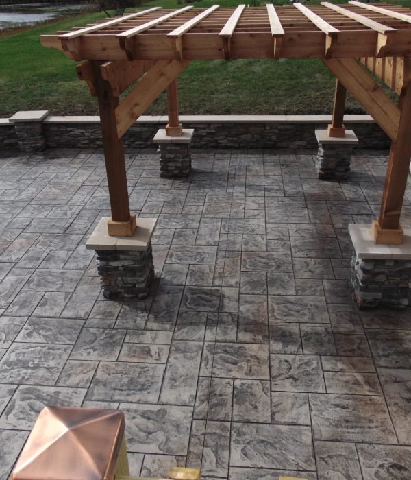Concrete patio with rustic wood pergola and stone columns, offering shaded outdoor space for dining or lounging.
