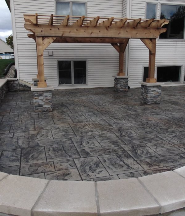 Elegant stamped concrete patio with a wood pergola and decorative seat wall, ideal for stylish backyard gatherings.